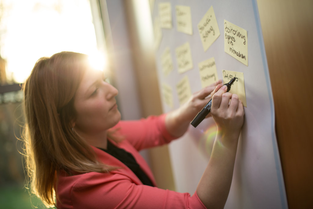 Frau schreibt mit Edding an Flipchart auf ein Post-it